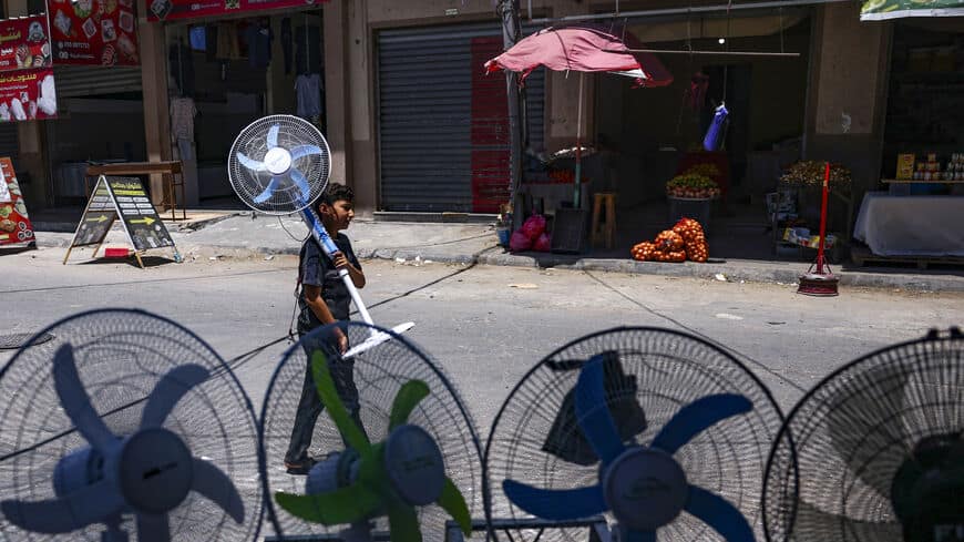 طفل صغير يحمل مروحة تعمل بالبطارية إلى المنزل وسط موجة حر ونقص في الكهرباء في مدينة غزة
