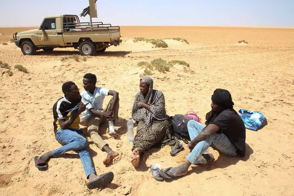 طفلة عمر ، ممرضة حامل تبلغ من العمر 26 عامًا من السودان ، تتحدث إلى مجموعة من الرجال حيث تقطعت بهم السبل في الصحراء على الحدود الليبية التونسية